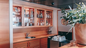 Une cuisine avec des armoires en bois, un évier et un plan de travail. On peut y voir différentes bouteilles et un verre à vin posés sur le plan de travail.