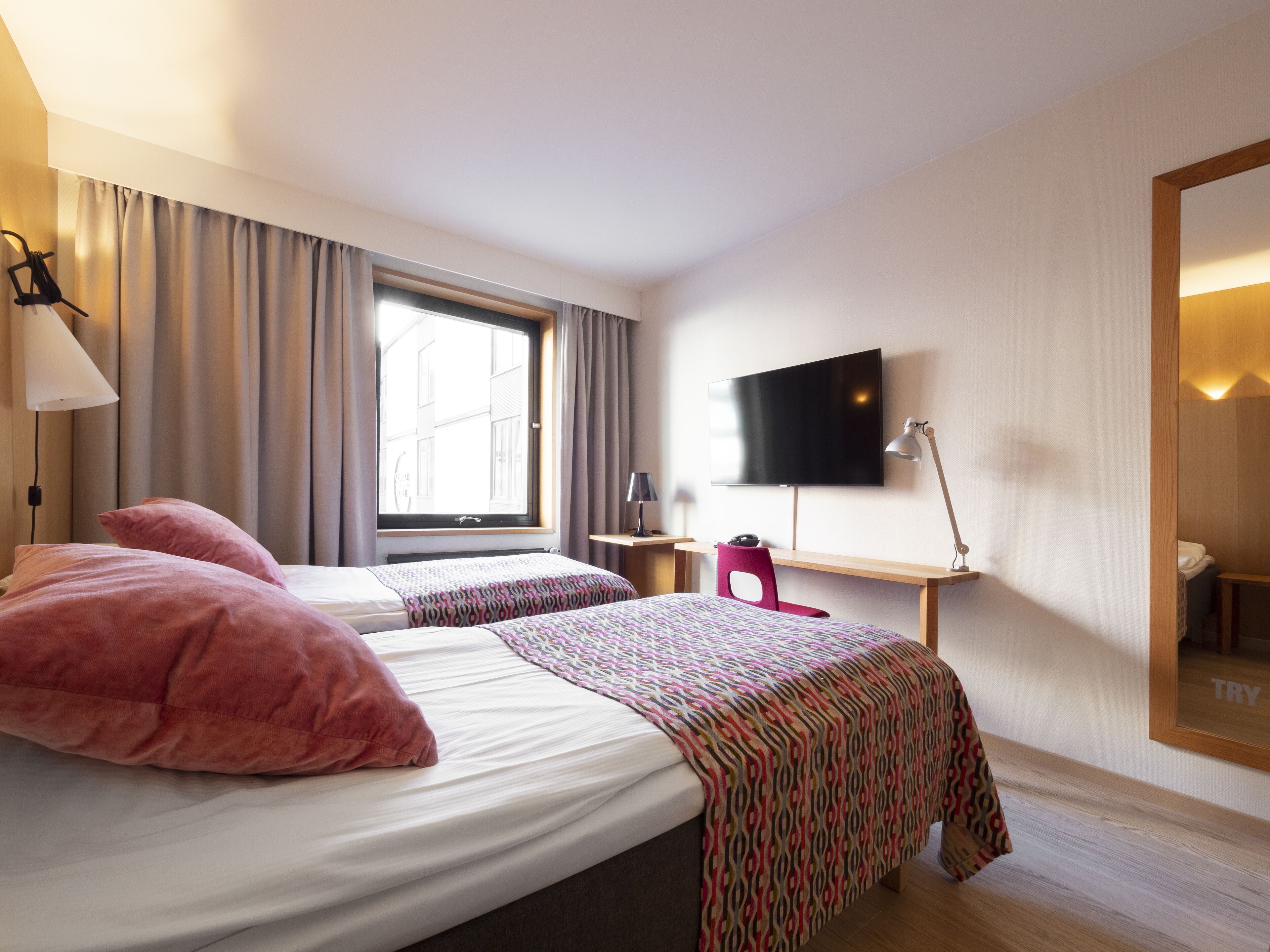 Una habitación de hotel con dos camas, televisión, escritorio y espejo.