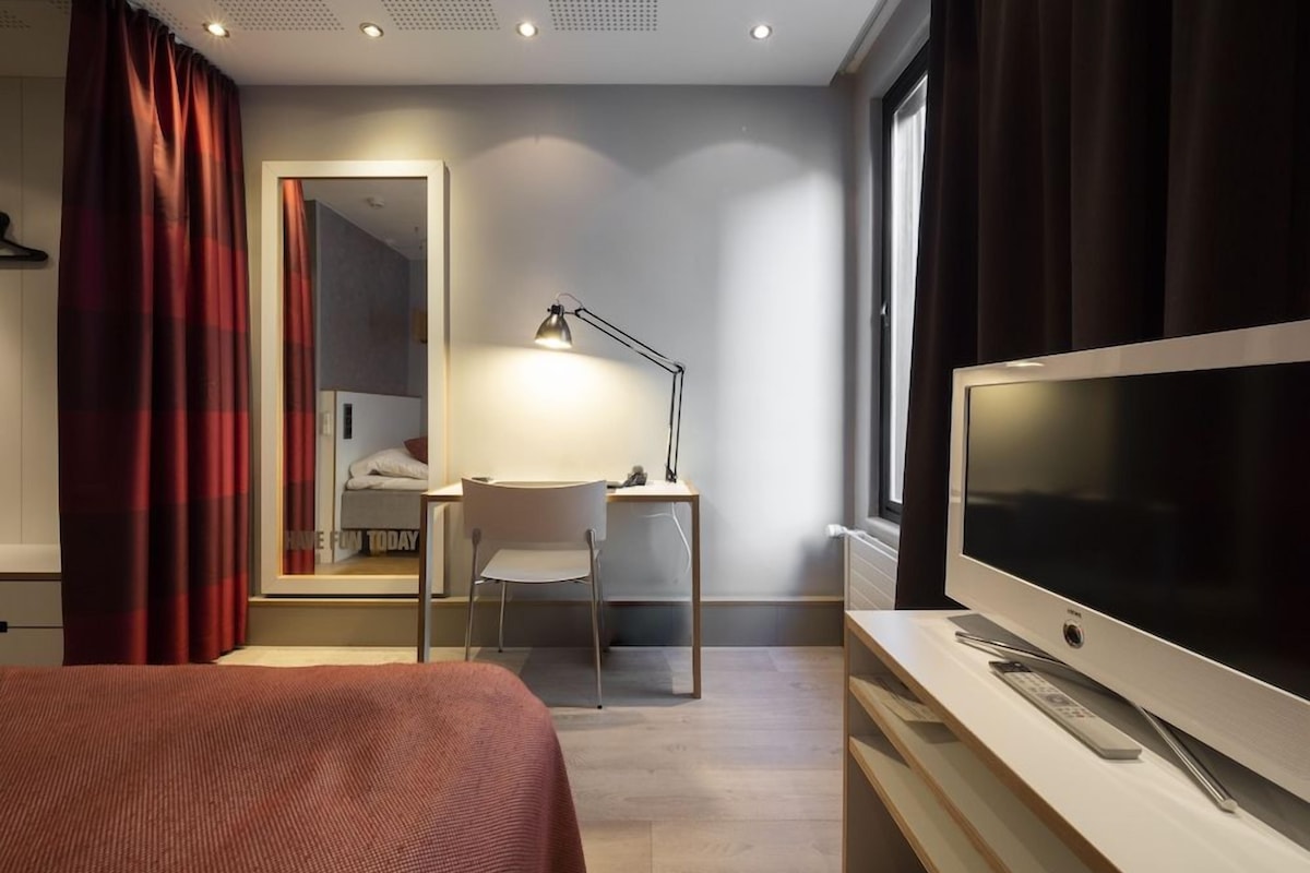 A hotel room with a bed, a desk, a chair, a television, and a window.