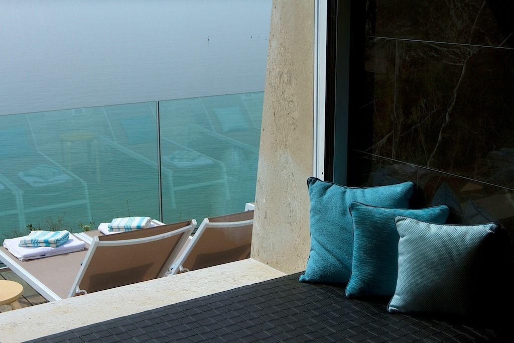 Ein Balkon mit Lounge-Möbeln und einem kleinen Tisch, ein großes Fenster mit Ausblick und eine strukturierte Wand.