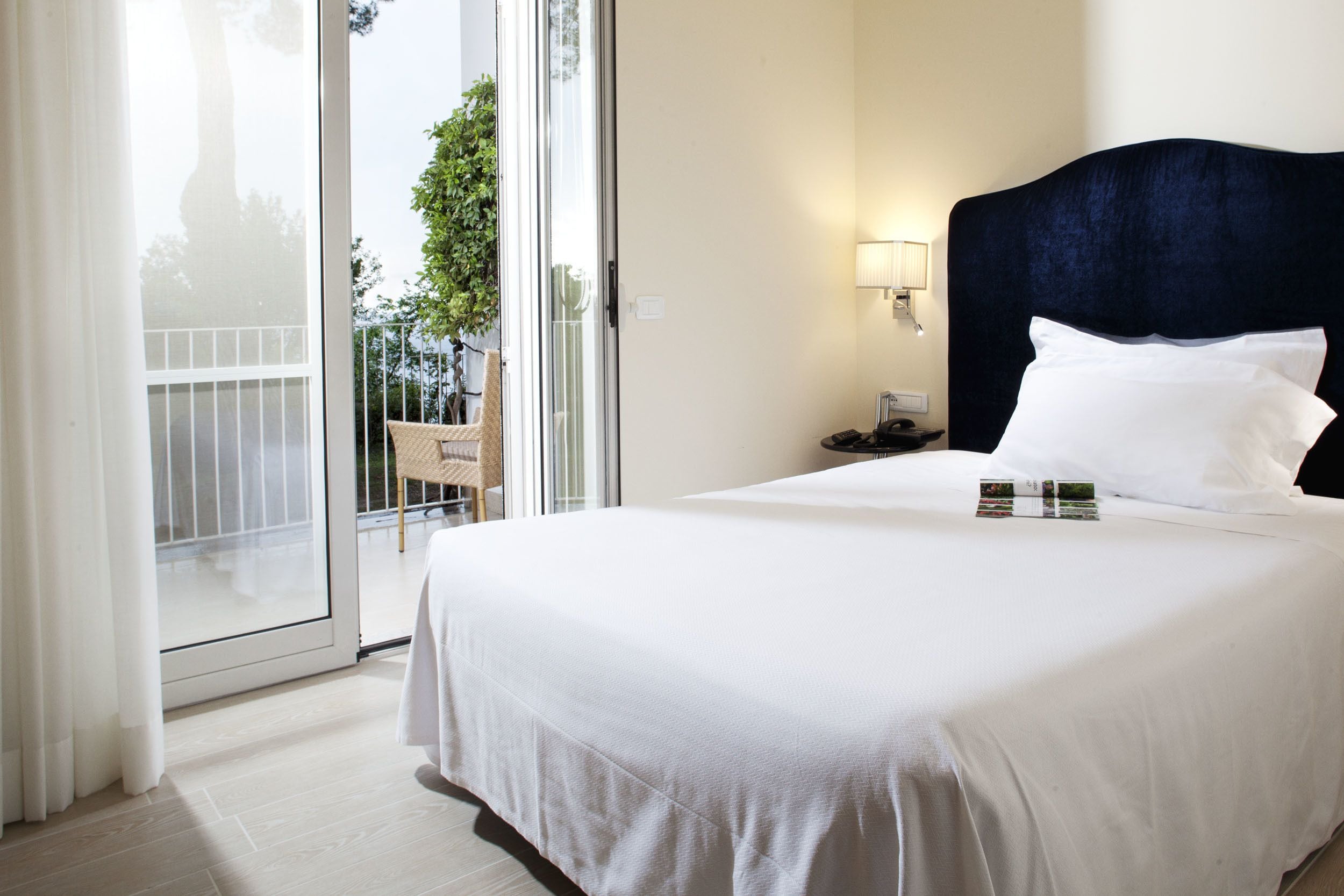 Camera d'albergo con un letto grande, un comodino, una lampada e vista all'esterno tramite una porta scorrevole in vetro.