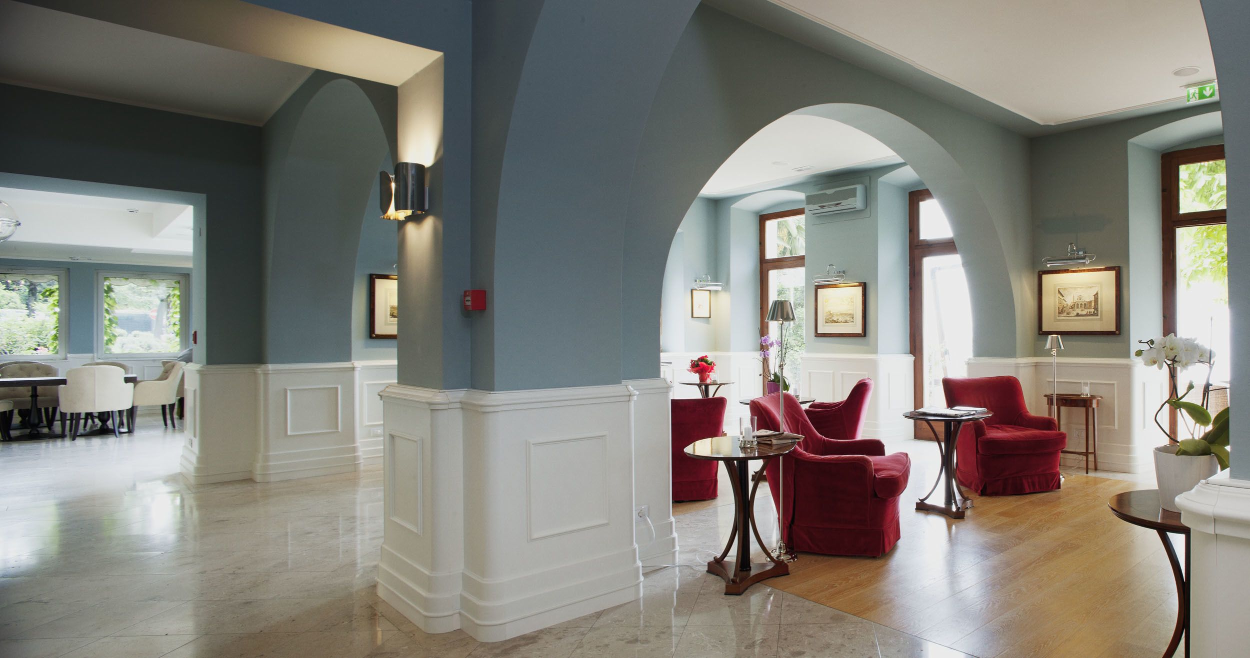 A spacious lobby with a marble floor, red upholstered chairs, and a dining area with white chairs.