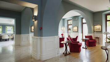 A spacious lobby with a marble floor, red upholstered chairs, and a dining area with white chairs.