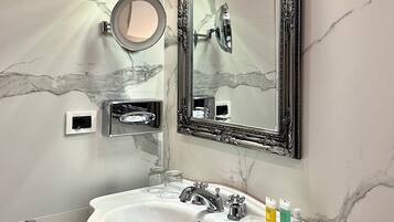 Un bagno con parete in marmo, uno specchio grande, un lavabo con accessori cromati e un portasciugamani.