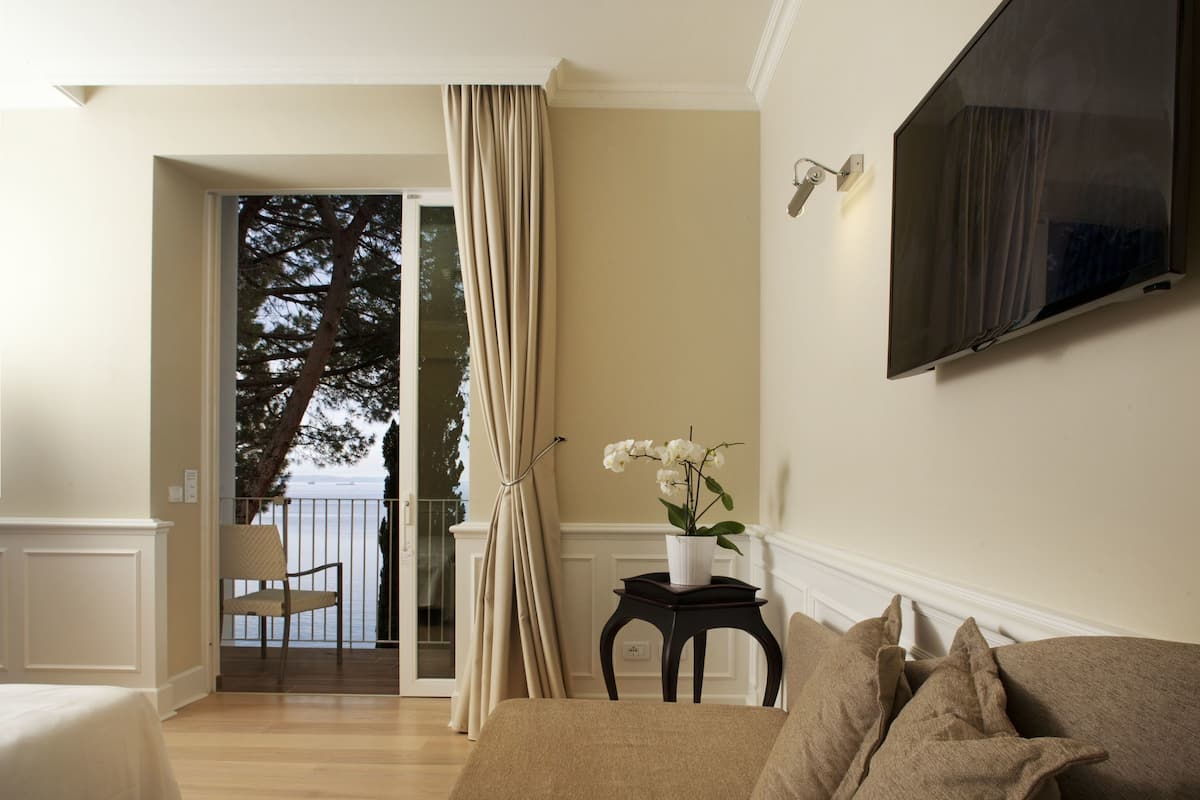 Un salon comprenant un canapé, une petite table sur laquelle est posé un vase de fleurs, un téléviseur fixé au mur et une vue sur un balcon avec une chaise.