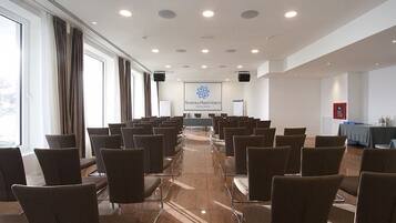 Un salón de conferencias con filas de sillas, una pantalla de proyección y una mesa cubierta con un mantel azul.