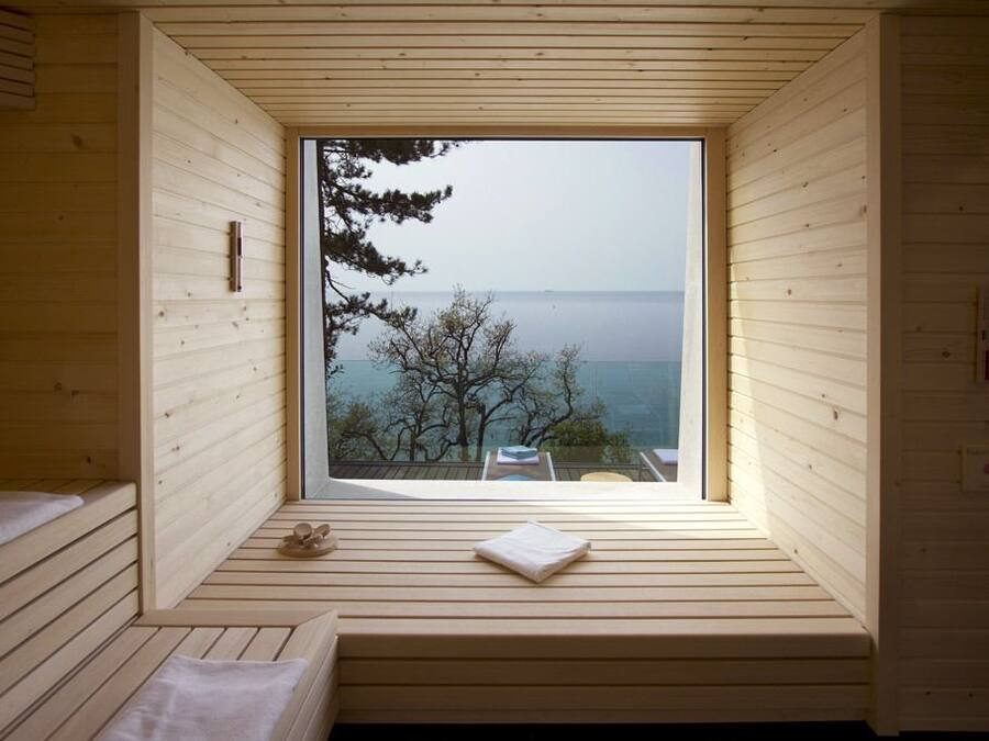 Una cabaña de madera con ventana que ofrece vistas a árboles y al mar.