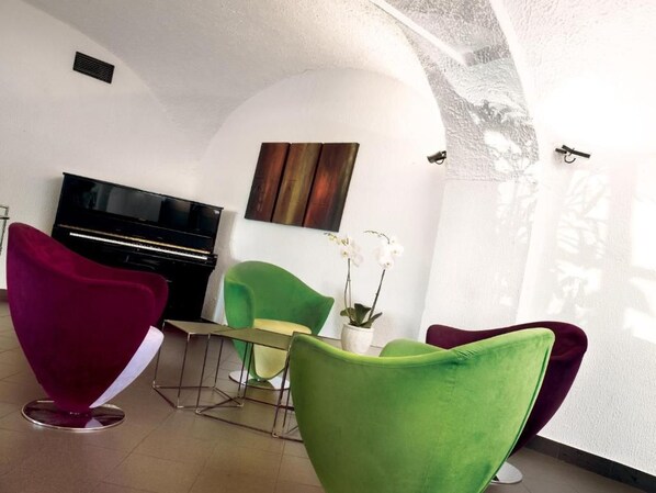 A room with a piano, a television, and two green chairs.