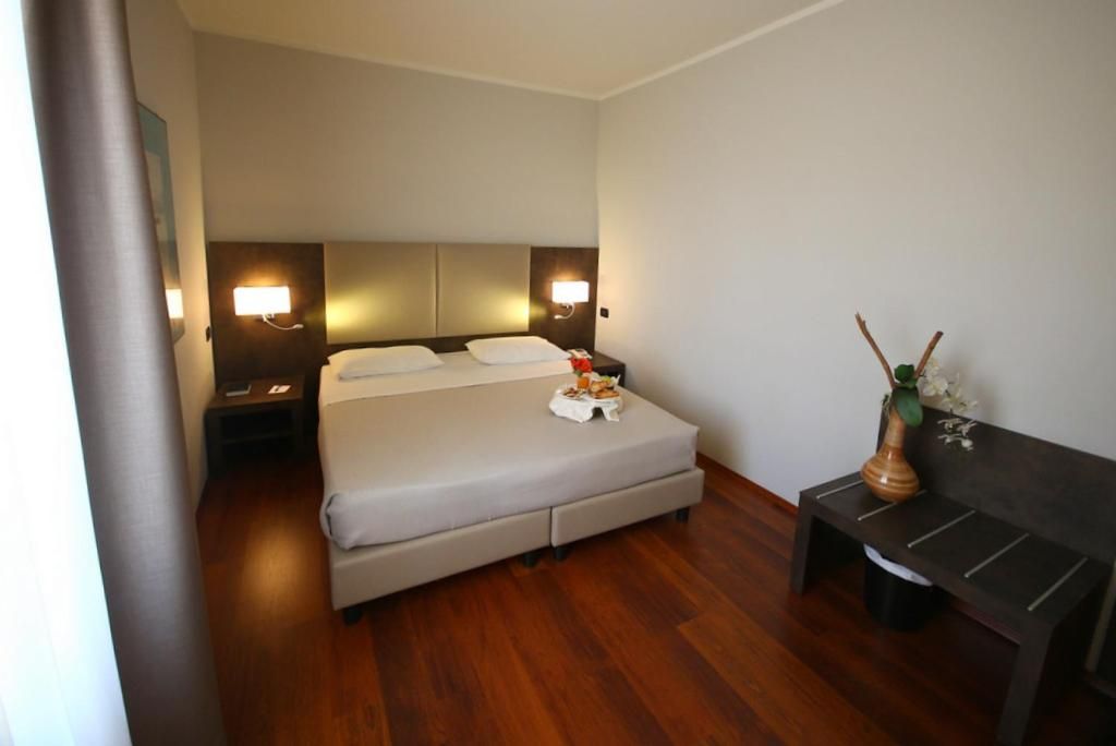 A hotel room with a bed, bedside tables, a bench, and a vase with flowers.