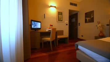Ein Hotelzimmer mit einem Bett, einem Schreibtisch mit Stuhl, einem Fernseher und einer Blumenvase.