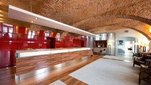 A spacious lobby with a wooden ceiling, a reception desk with a red finish, and a seating area with a patterned rug.