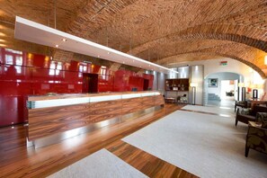 A spacious lobby with a wooden ceiling, a reception desk with a red finish, and a seating area with a patterned rug.