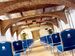 A hotel interior with rows of blue chairs, a brick ceiling, and a plant in the background.