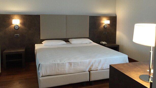 A hotel room with a large bed, two bedside tables, a nightstand, and a lamp.