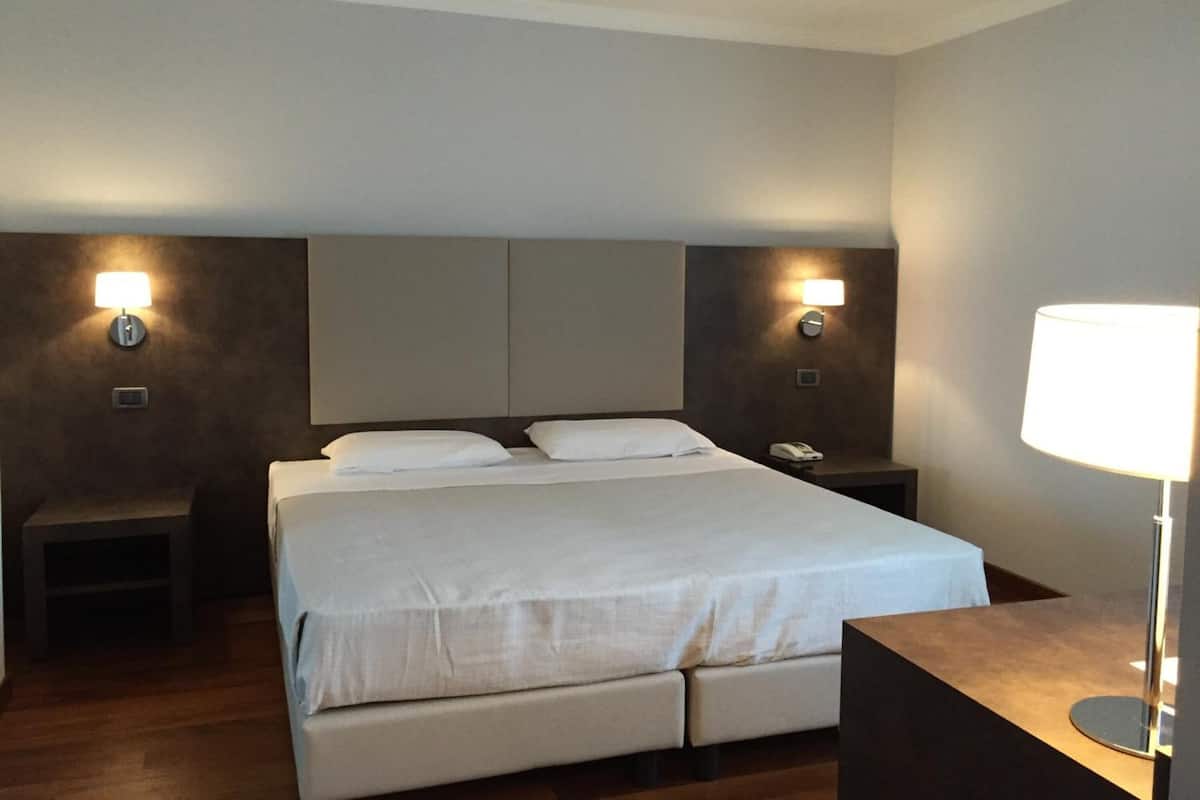Una habitación de hotel con una cama grande, dos mesitas de noche y una lámpara.