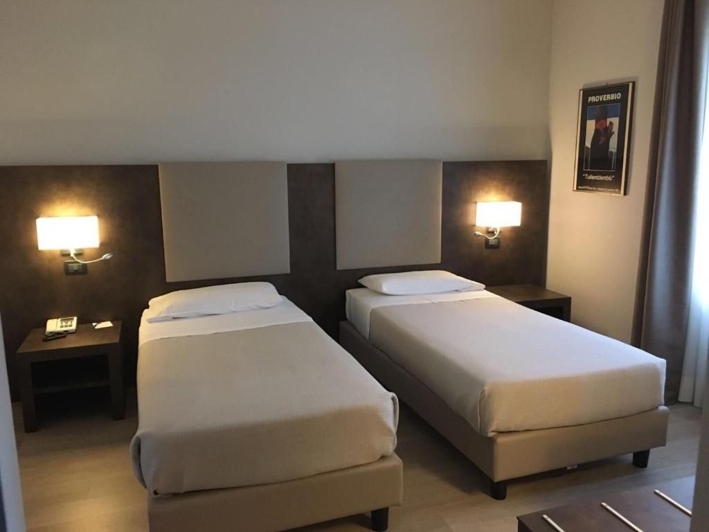 Una camera d'albergo con due letti singoli, comodini, lampade e un quadro appeso al muro.