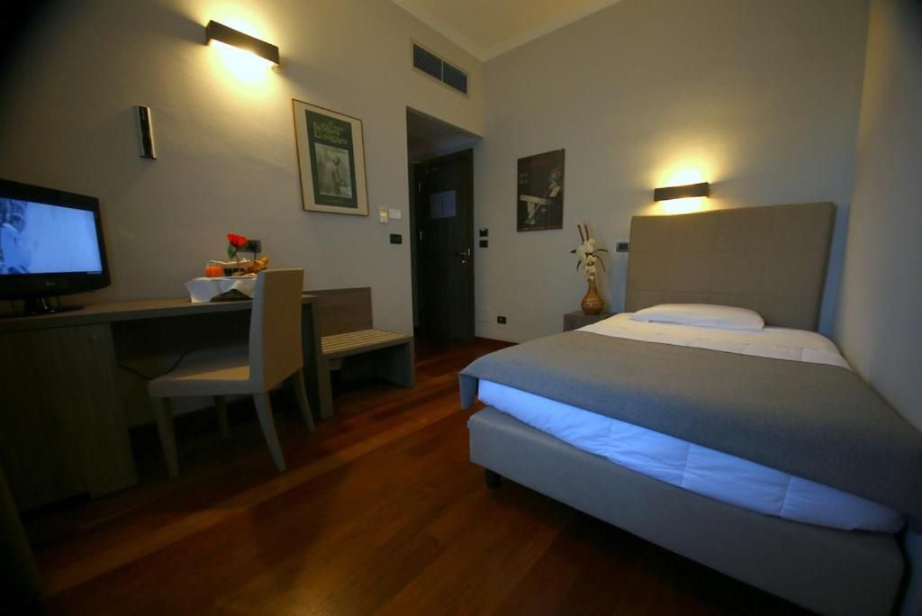 A hotel room with a bed, desk, chair, and a television.