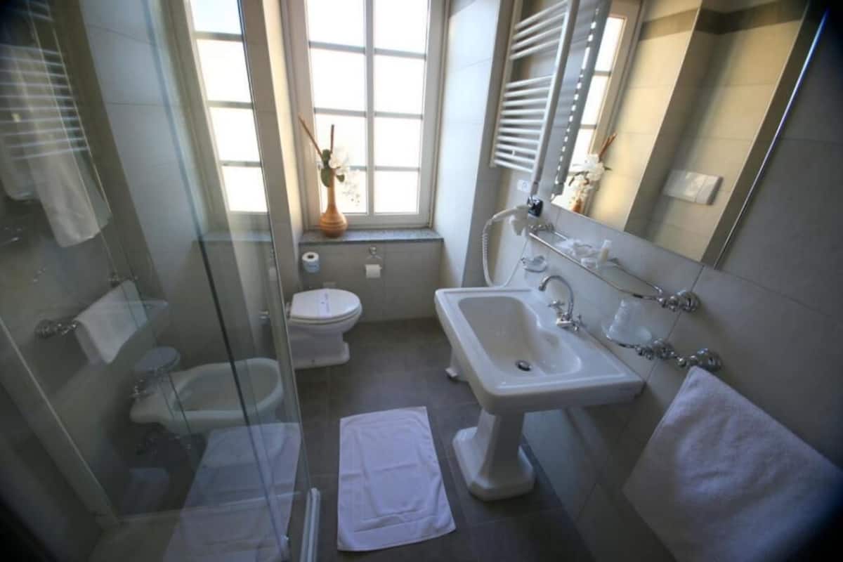 Un baño moderno con cabina de ducha de vidrio, lavamanos pedestal y retrete.