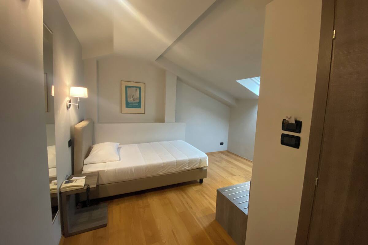 Un dormitorio con cama, mesita de noche, lámpara y un cuadro en la pared.