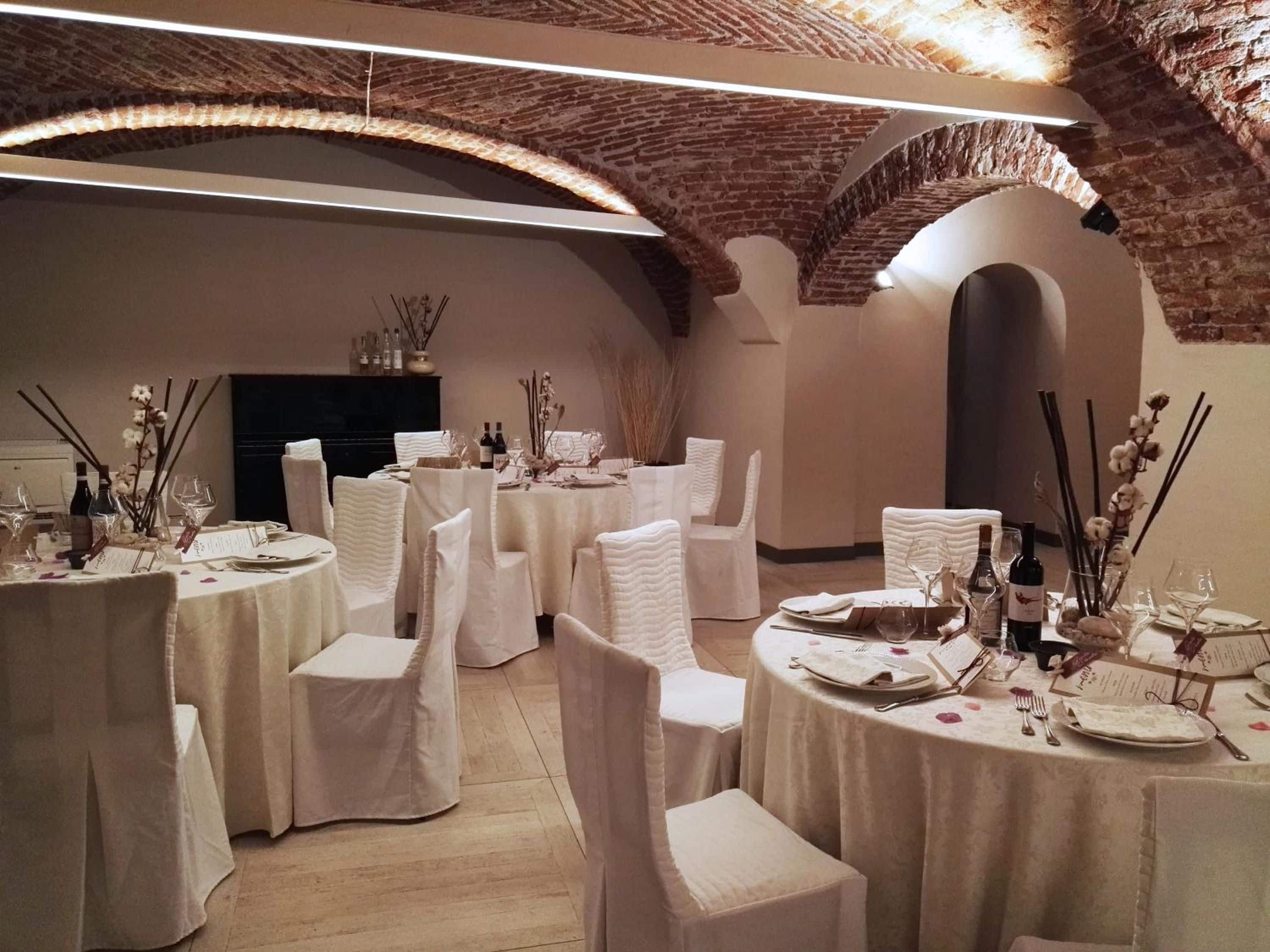 Ein Festsaal mit runden Tischen, weißen Stühlen und einer Ziegeldecke.