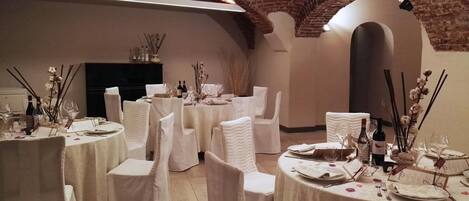 A banquet hall with round tables, white chairs, and a brick ceiling.