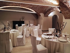 Un salón de banquetes con mesas redondas, sillas blancas y techo de ladrillo.