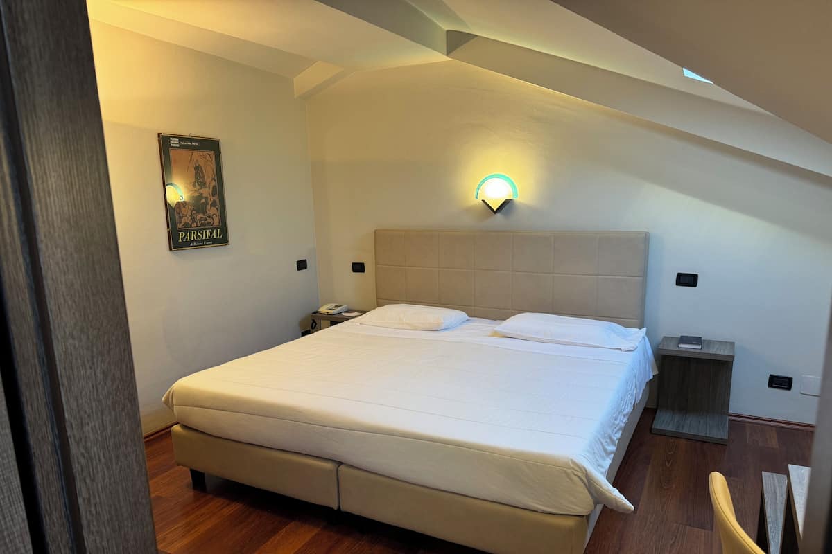 Un dormitorio con una cama grande, una mesita de noche, una lámpara de pared y un cartel en la pared.