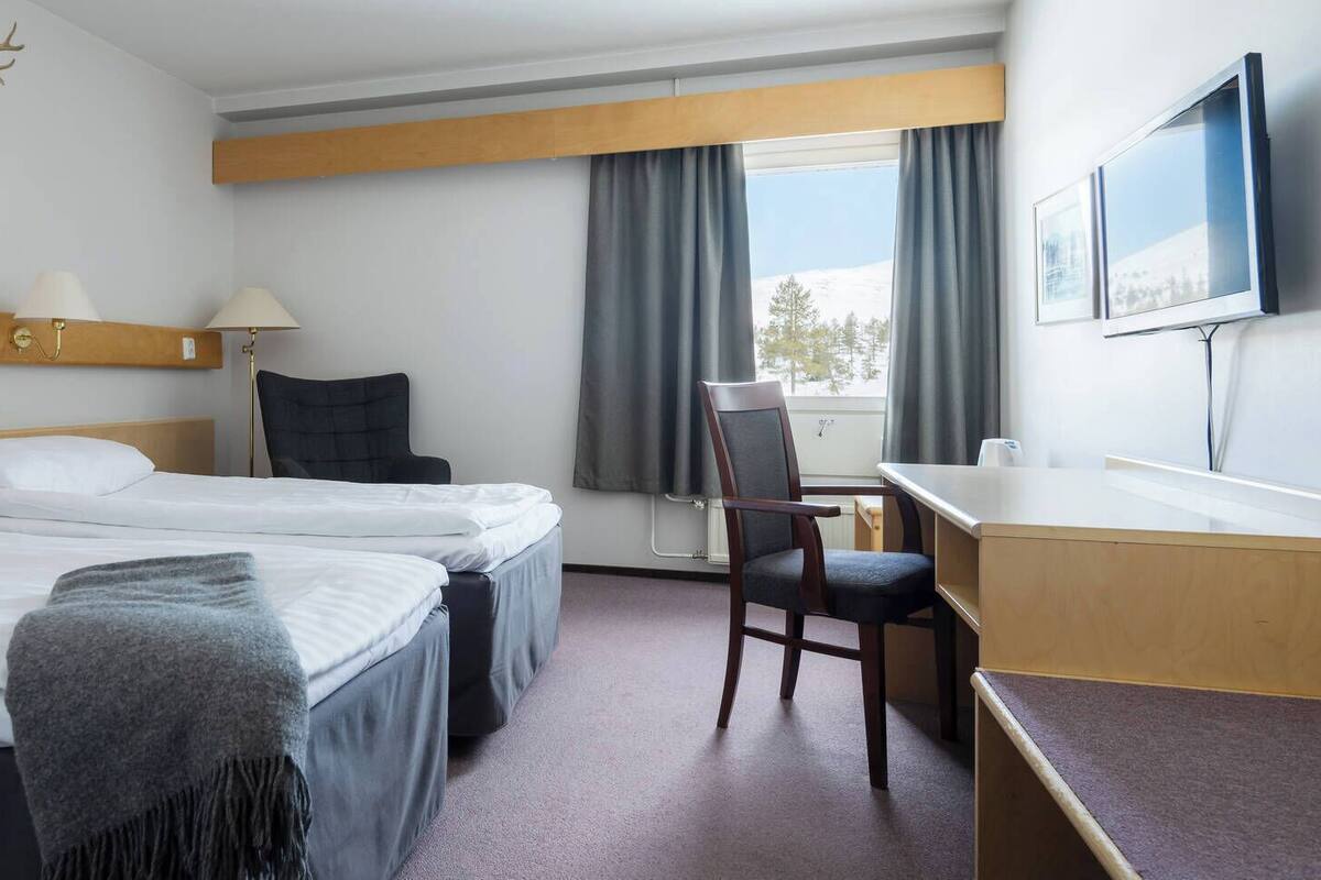 Hotelkamer met twee bedden, een bureau, een stoel, een televisie en een raam met gordijnen.