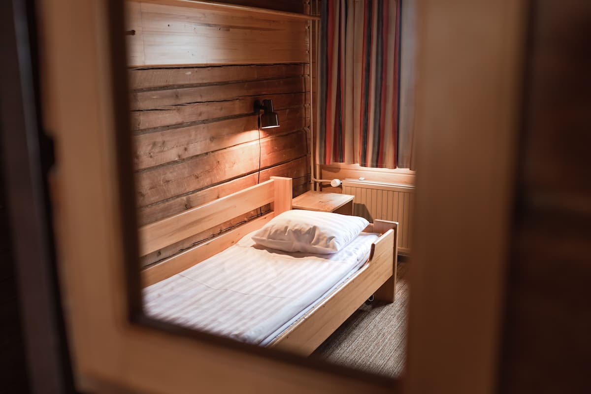 Een kleine houten kamer met een bed, een nachtkastje en een raam met gordijnen.