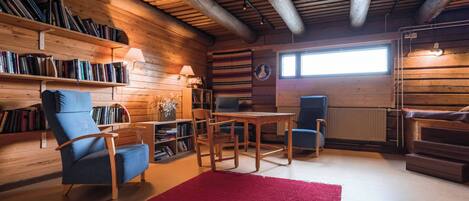 Ein gemütliches Blockhaus-Interieur mit Holzwänden, einer Bücherwand, einem Esstisch und einem roten Teppich.