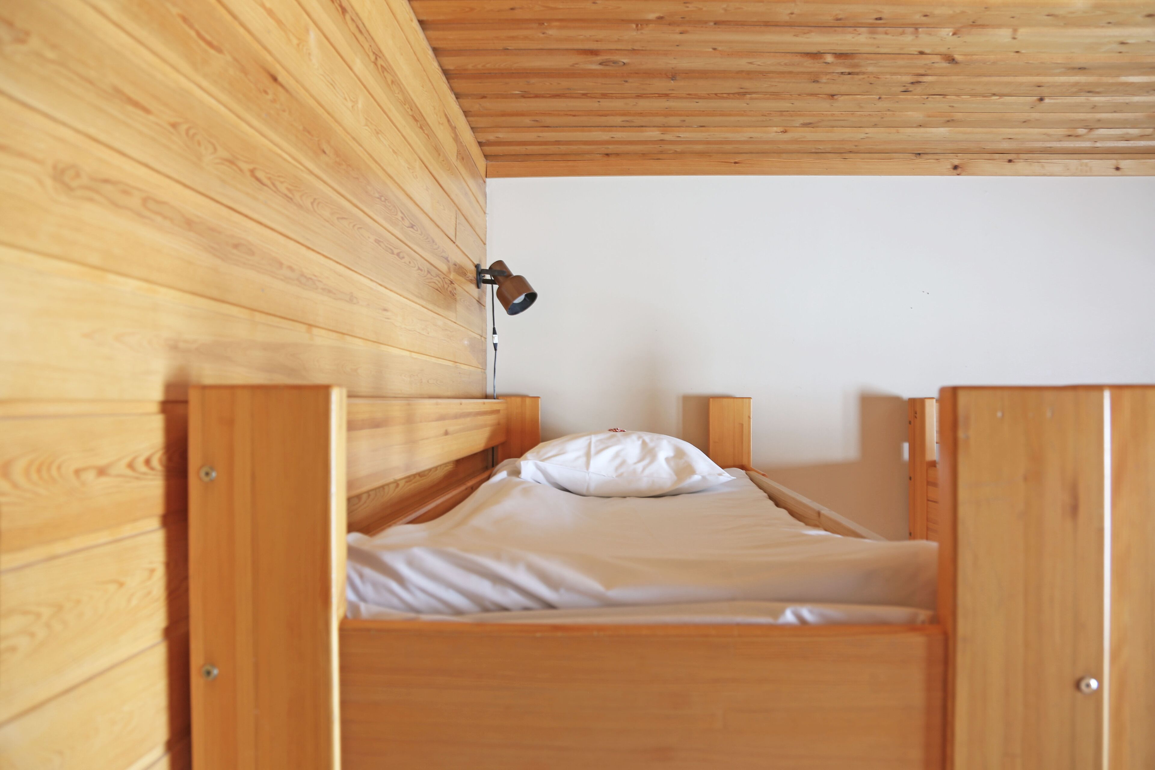 A single wooden bunk bed with a headboard, a bedside lamp, and a white pillow.