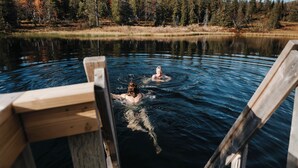 Une jetée en bois s’étendant au-dessus d’un lac paisible, où deux personnes se baignent.