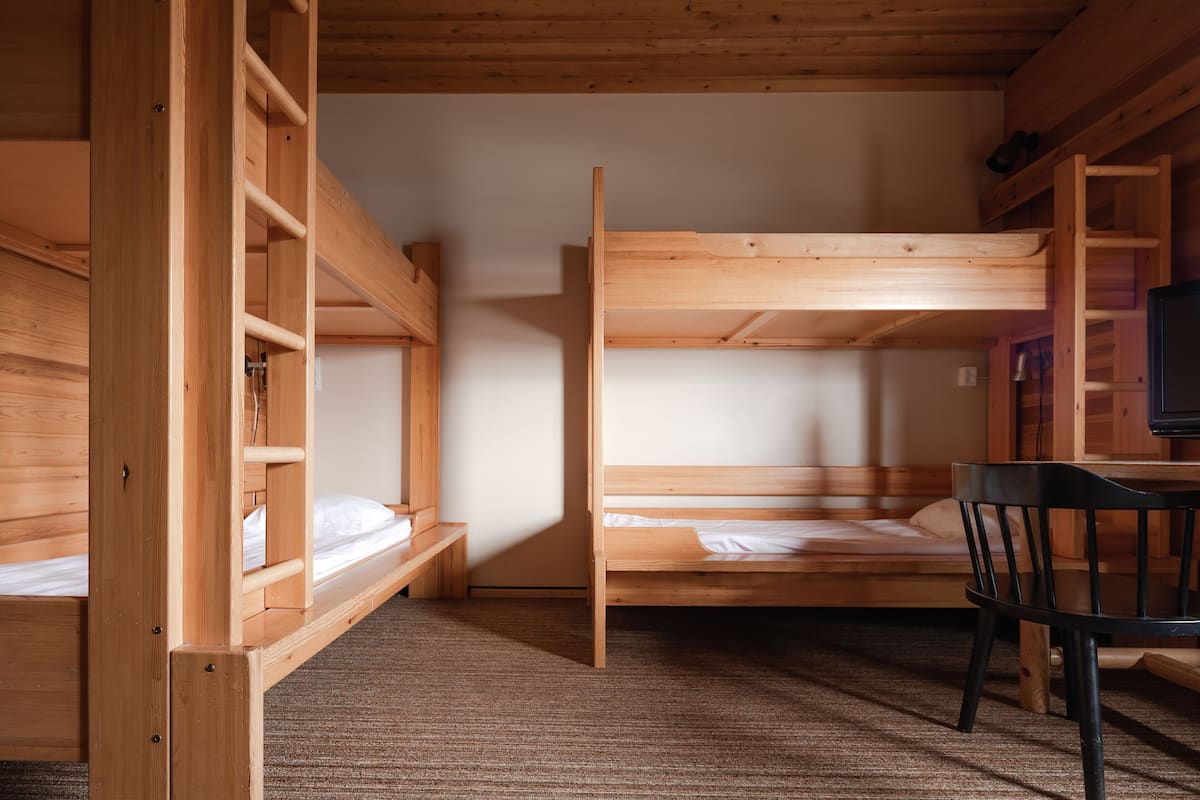 Een slaapkamer met een stapelbed, bureau en stoel, houten wanden en een vloerbedekking.