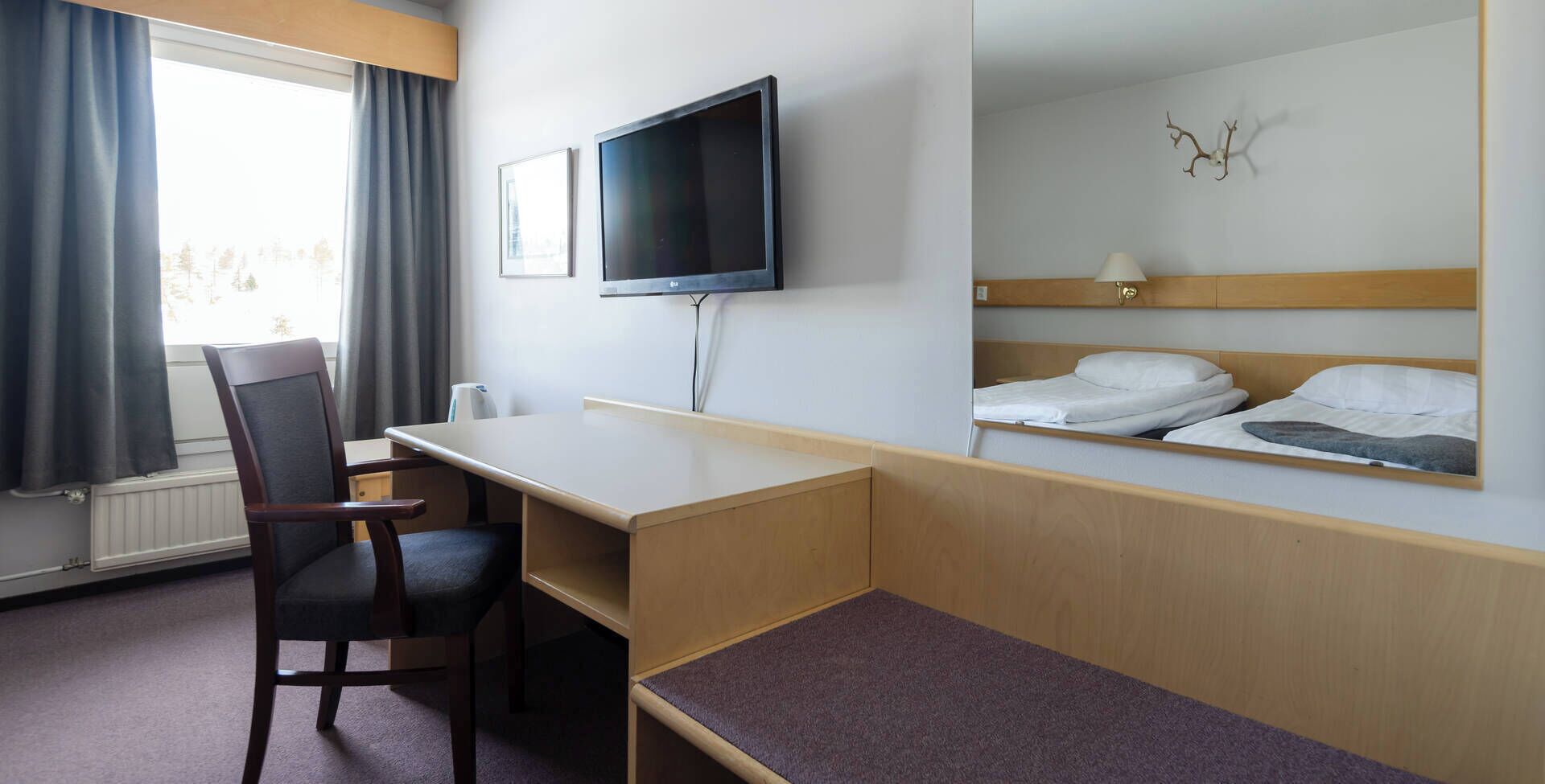Hotellihuone, jossa on sänky, työpöytä, tuoli, televisio ja ikkuna, jossa on verhot.