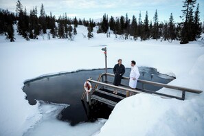 A wooden dock extending over a frozen pond with two people standing on it.
