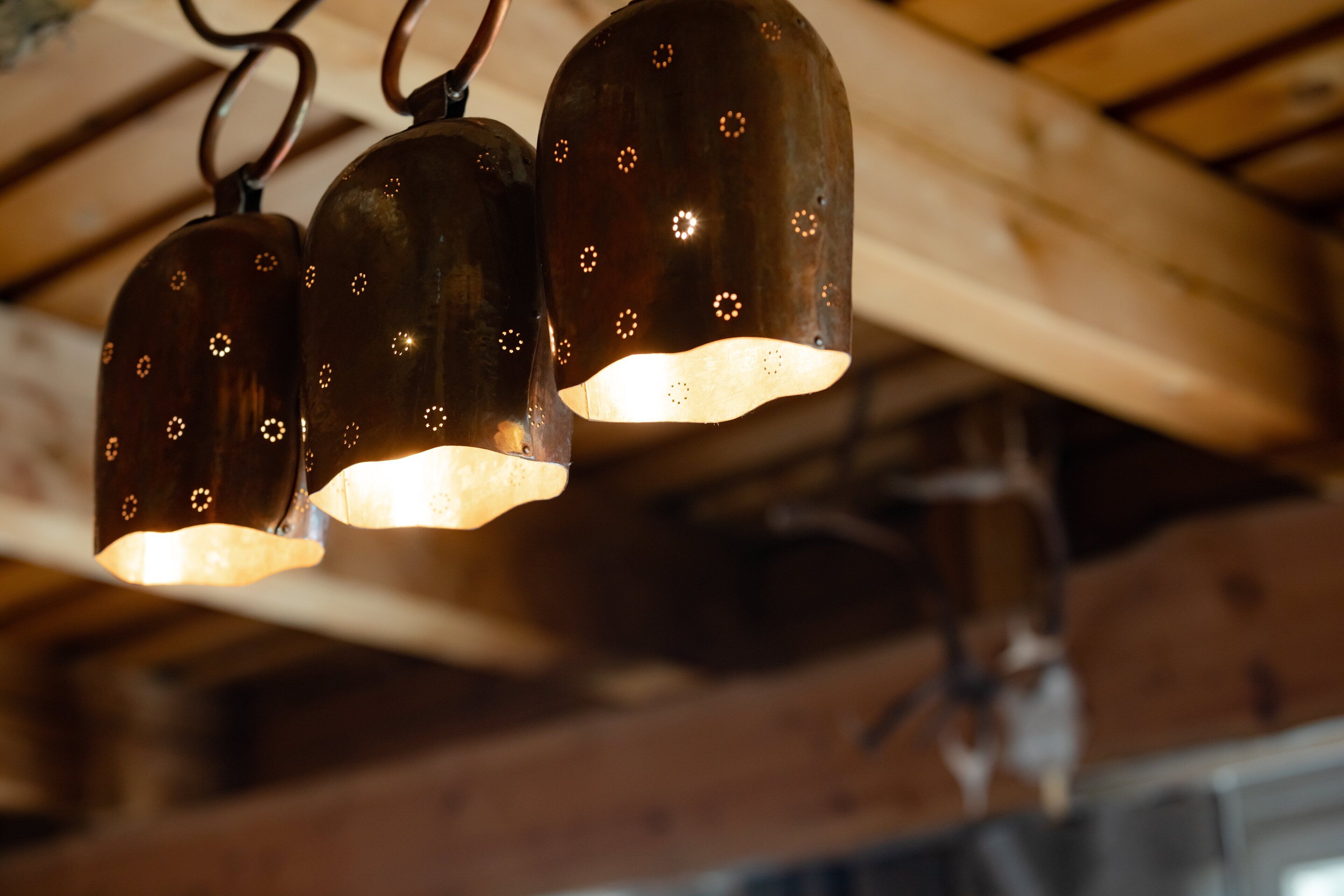 Gros plan de trois luminaires suspendus au design rustique, avec un plafond en bois et des poutres apparentes.