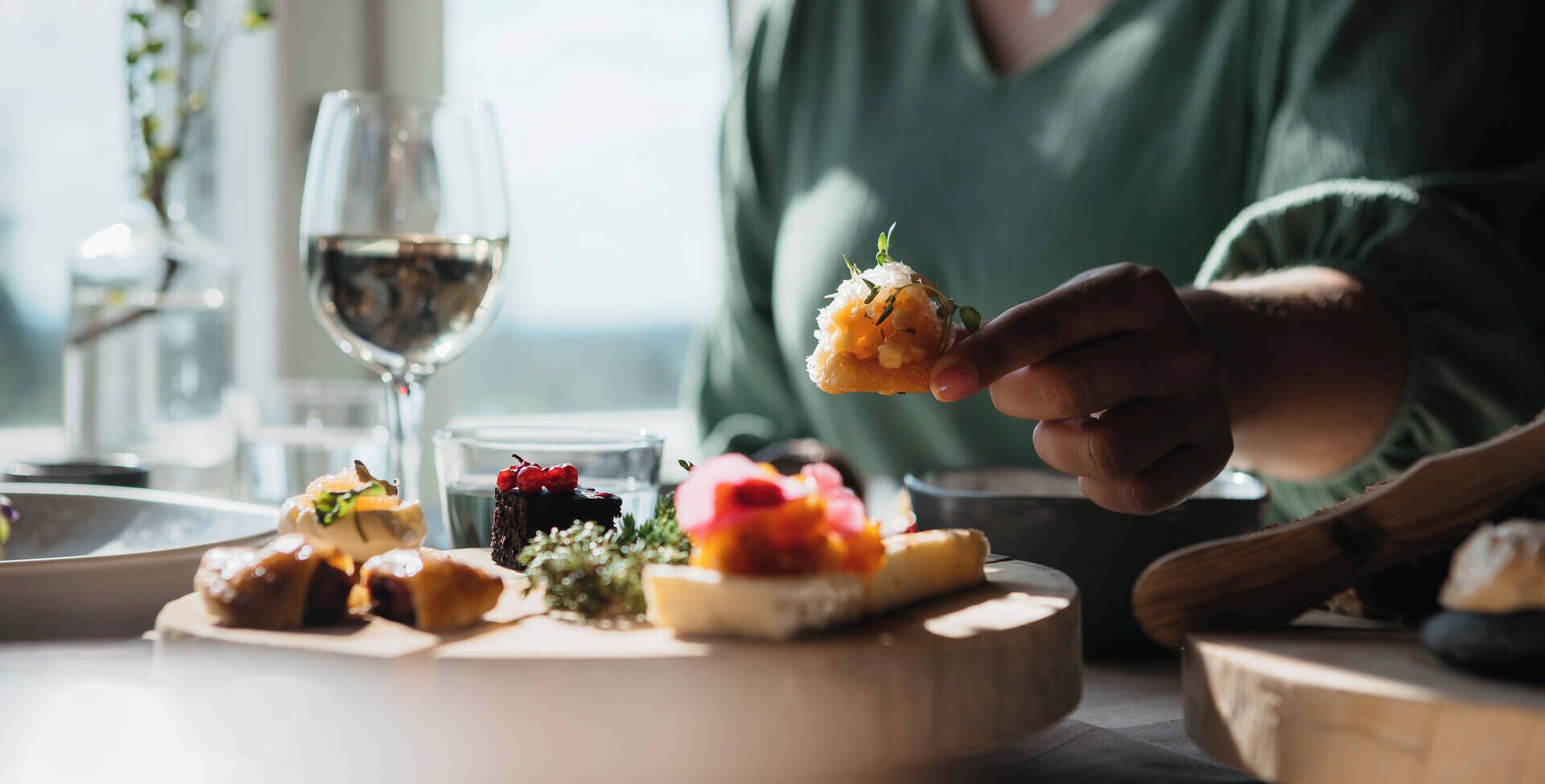 Una persona sostiene un alimento en una mesa con varios platos y una copa de vino.