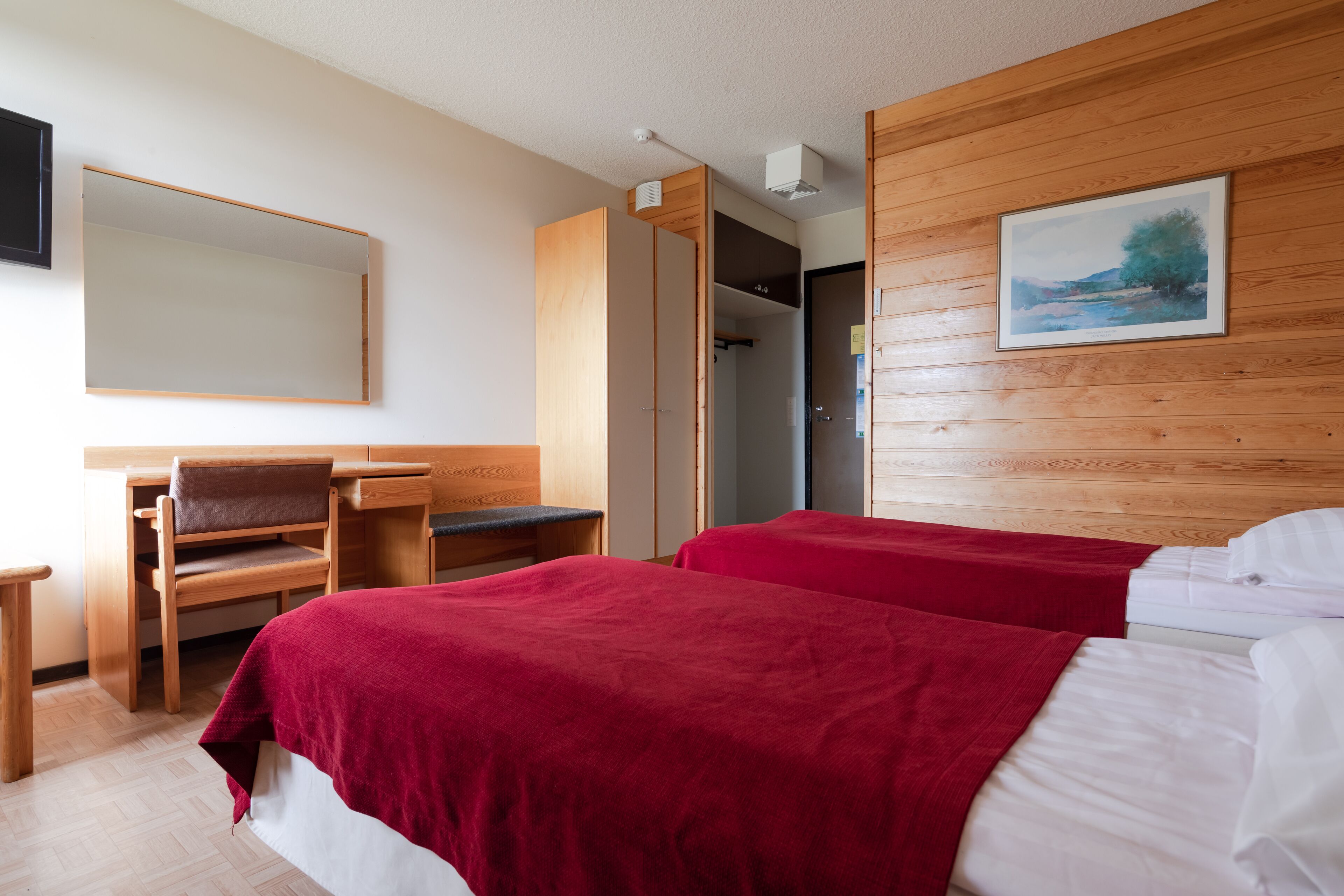 Habitación de hotel con dos camas, un escritorio, una silla y un espejo grande.