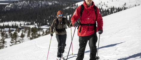 Dos personas esquiando en una pendiente nevada, con un bosque al fondo.