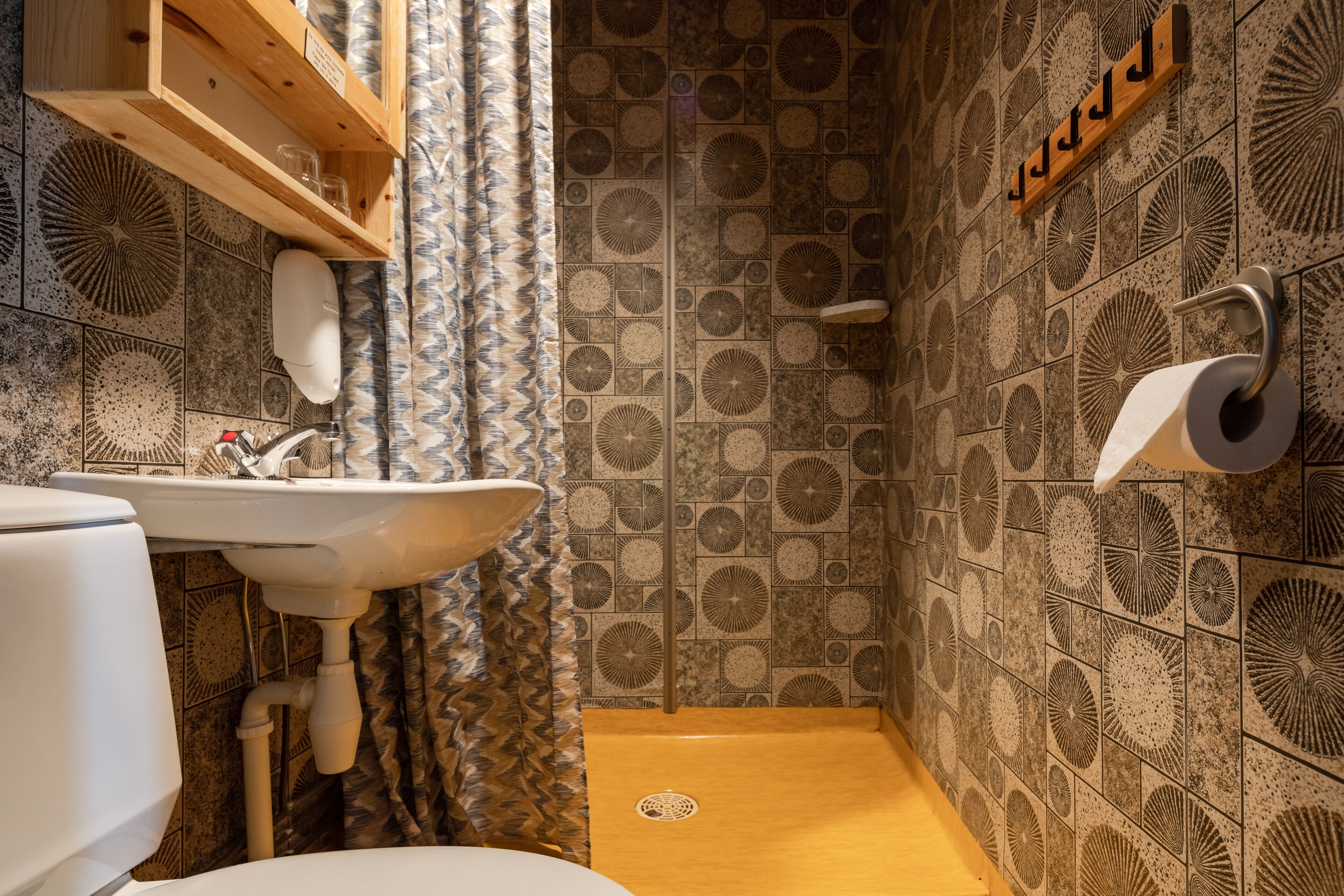 Un baño con lavamanos, inodoro, ducha y baldosas estampadas.