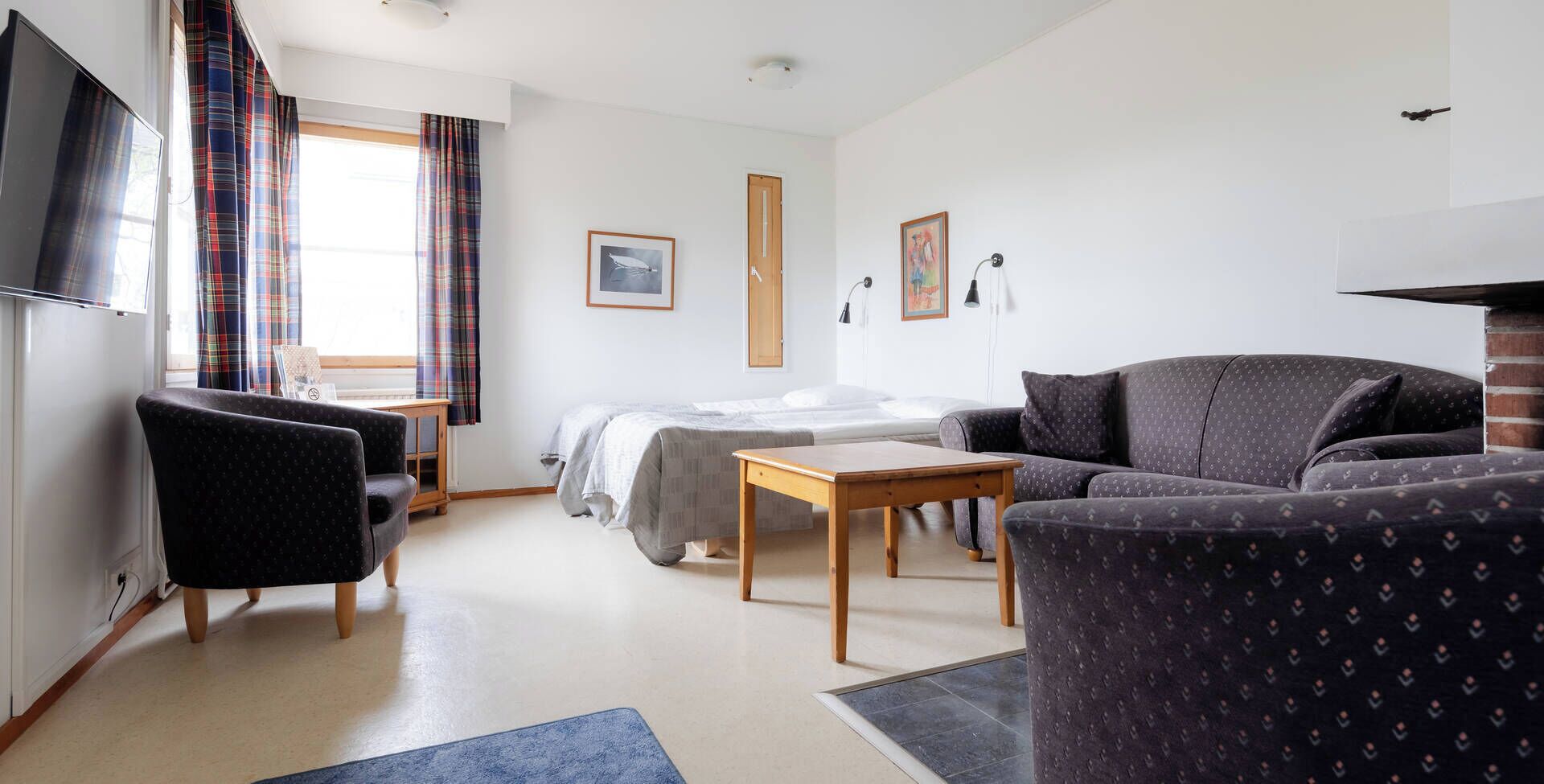 A modern hotel room with a bed, a sofa, a desk, and a TV.