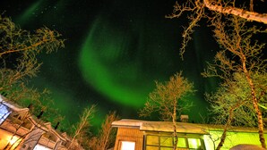 A cabin with a window and a door, surrounded by trees and a starry night sky. - Lapland Hotels Kilpis (Enontekio)