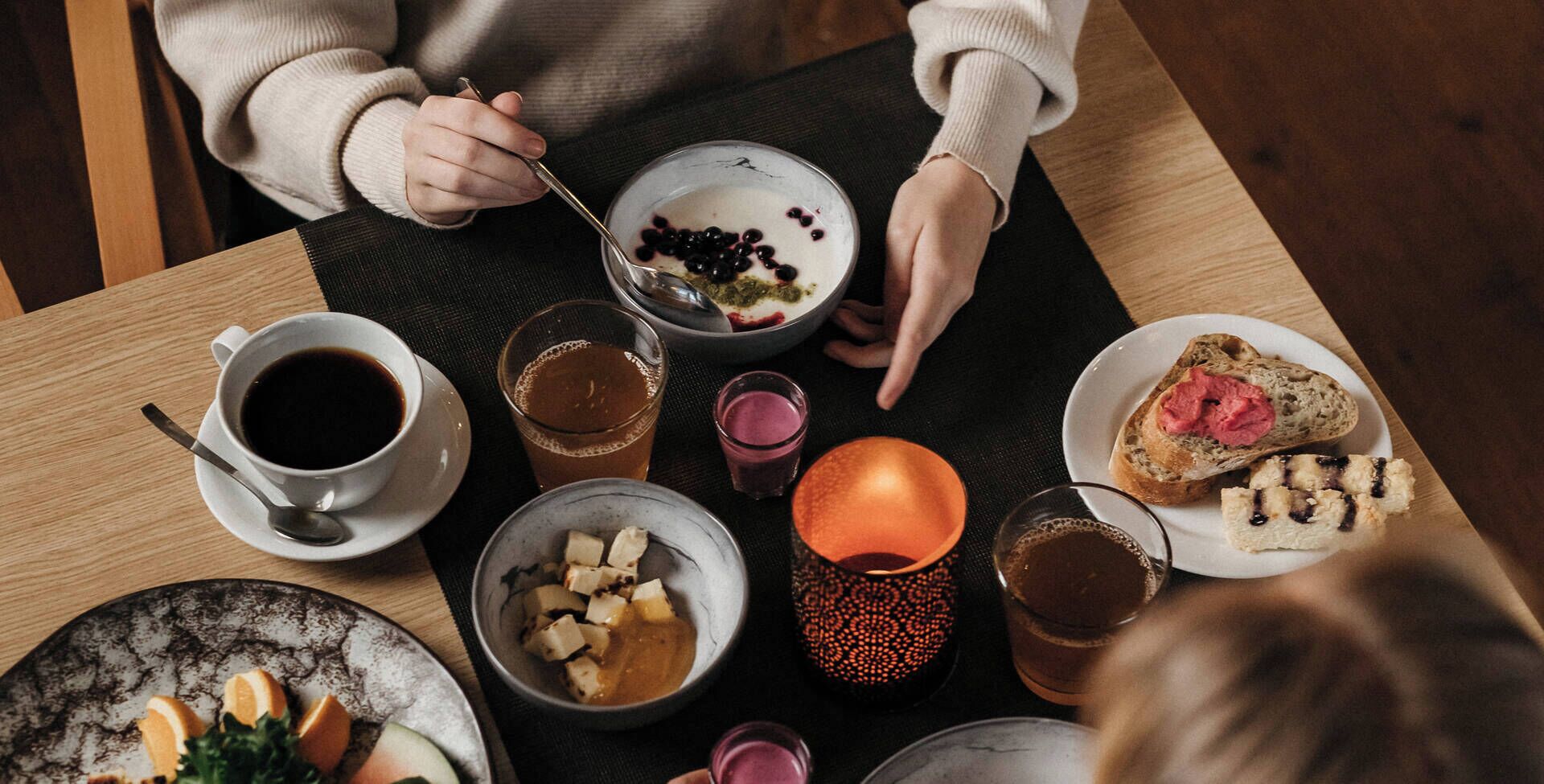 A dining table with various food items and drinks, including a bowl of yogurt with berries, a plate of toast with jam, and a cup of coffee.