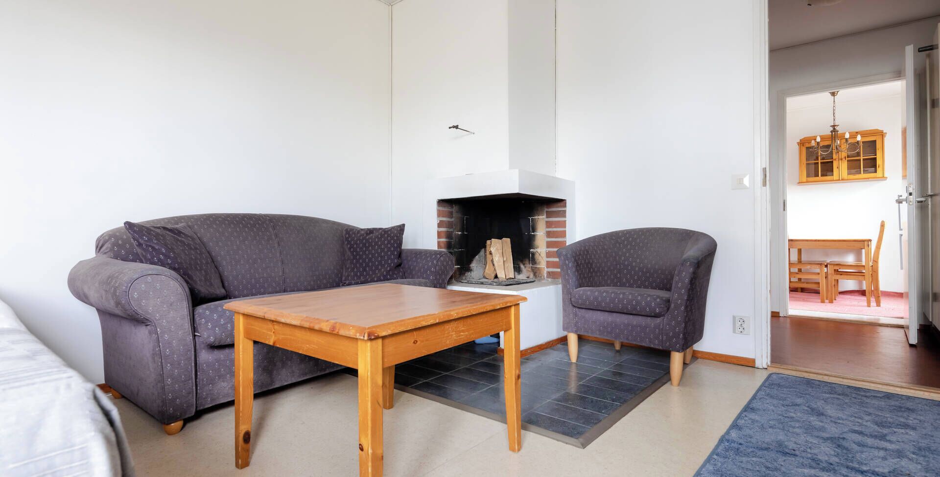 A living room with a sofa, two armchairs, a wooden coffee table, and a fireplace.