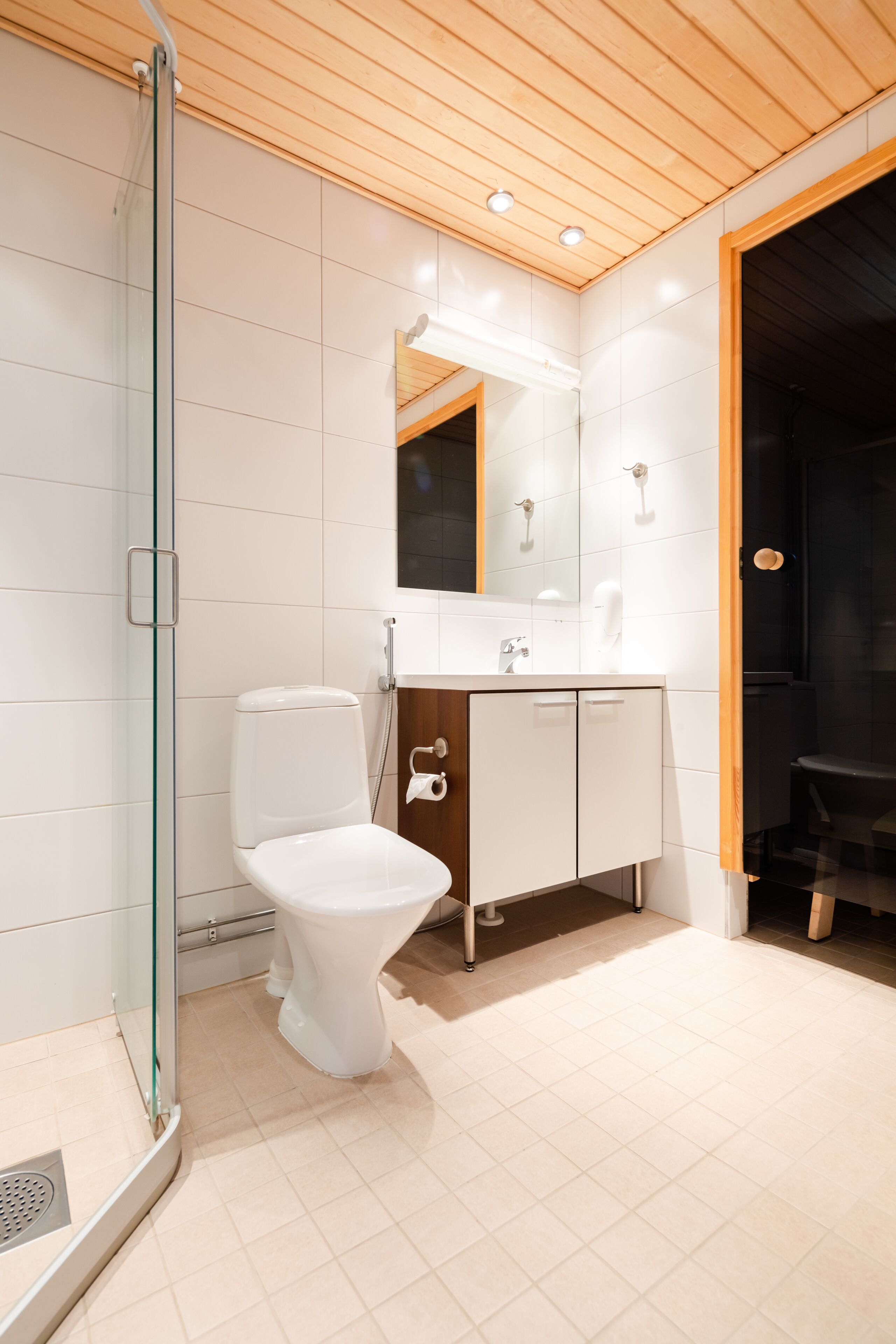 A modern bathroom with a glass shower enclosure, a white toilet, and a wooden vanity with cabinets.