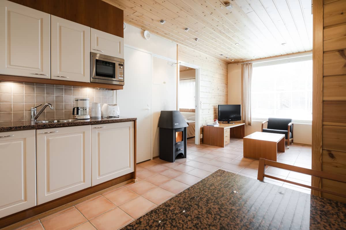 Una cocina moderna con armarios blancos, microondas y cafetera. Hay una chimenea, televisor y zona de estar con una mesa y sillas.
