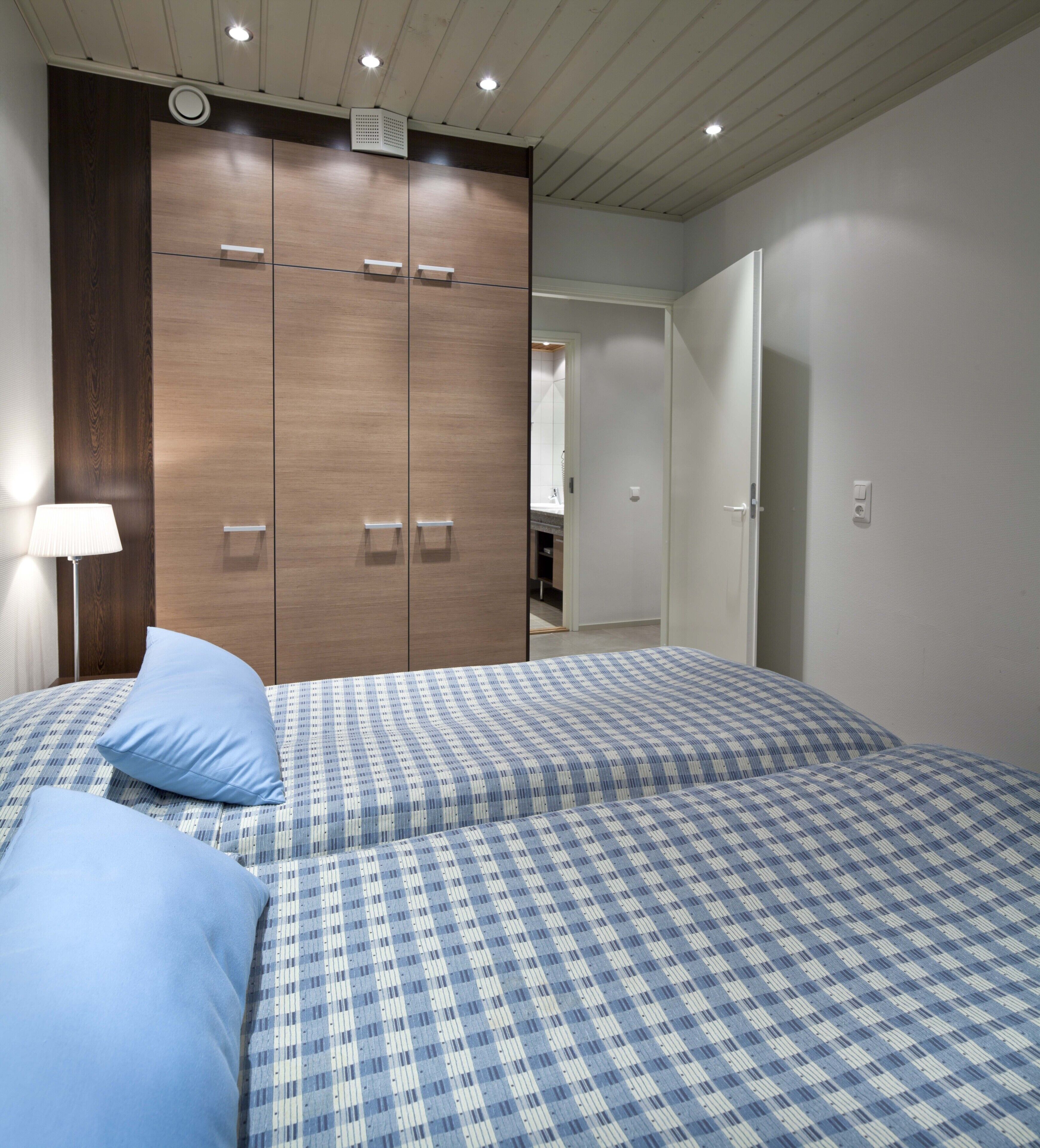 Ein Schlafzimmer mit großem Kleiderschrank, einem Bett mit karierter Bettwäsche und einem Nachttisch mit Lampe.