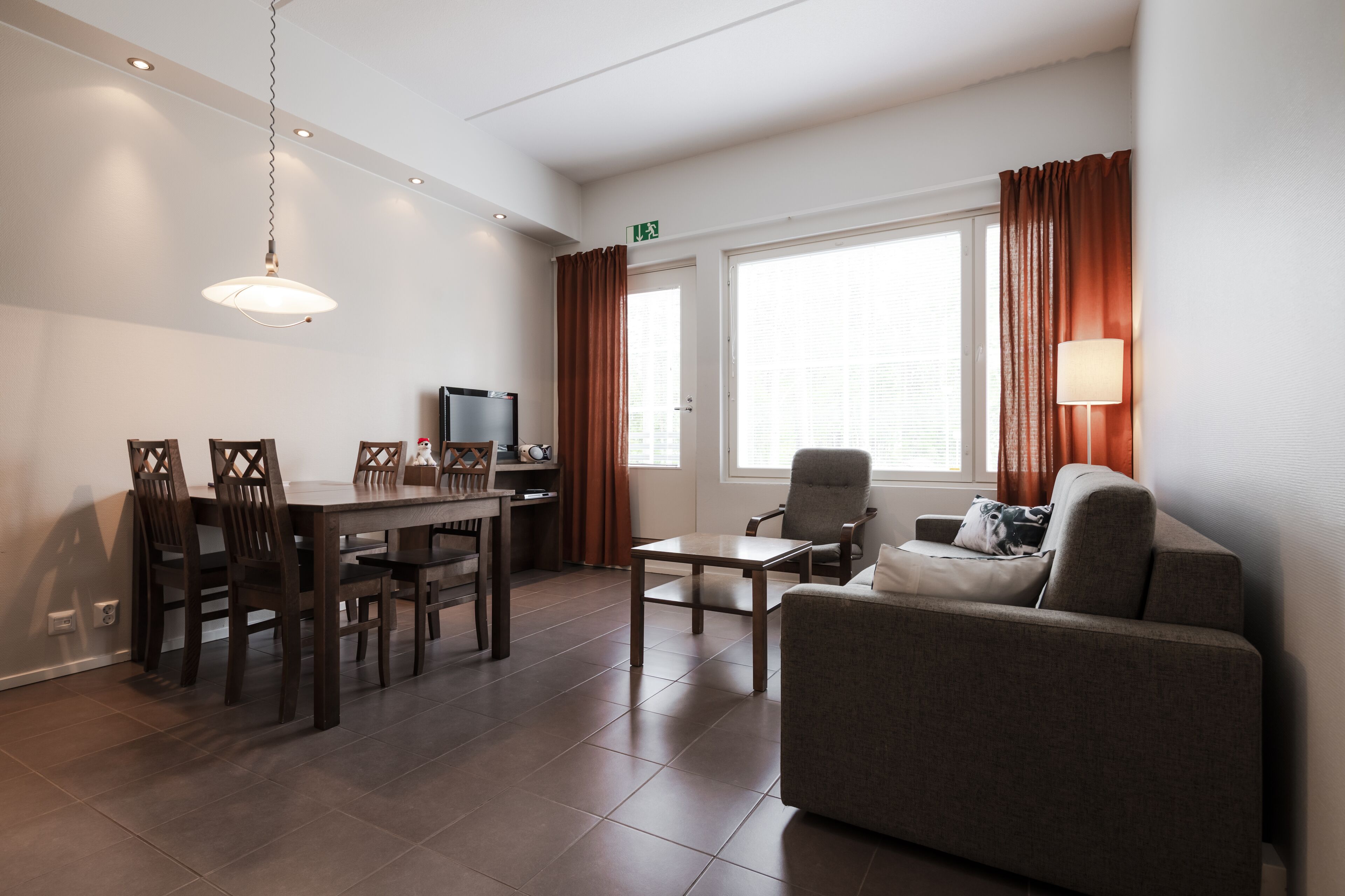 A modern living room with a sofa, a dining table with chairs, a TV, and a lamp.