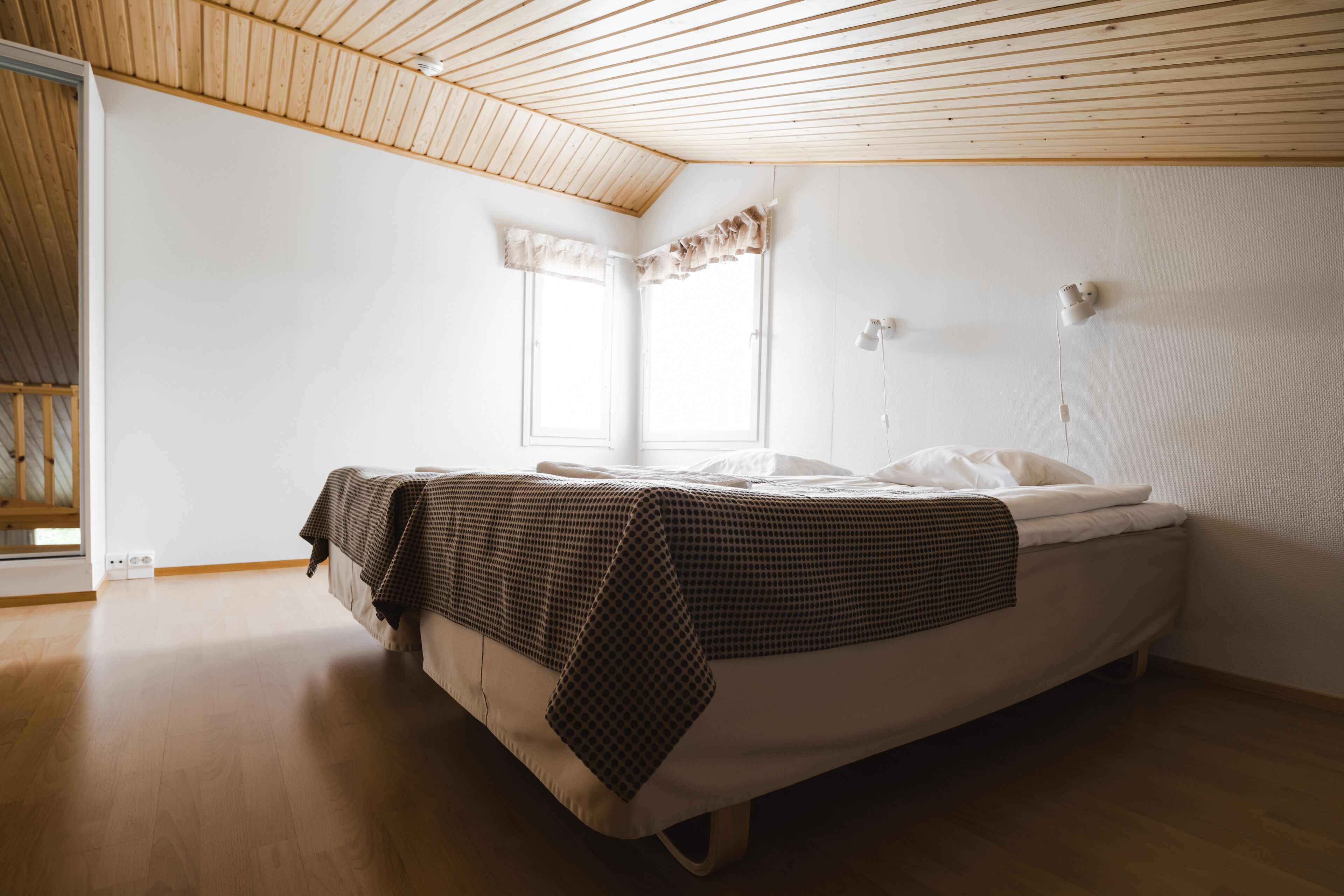 A bedroom with a bed, wooden ceiling, and a window.