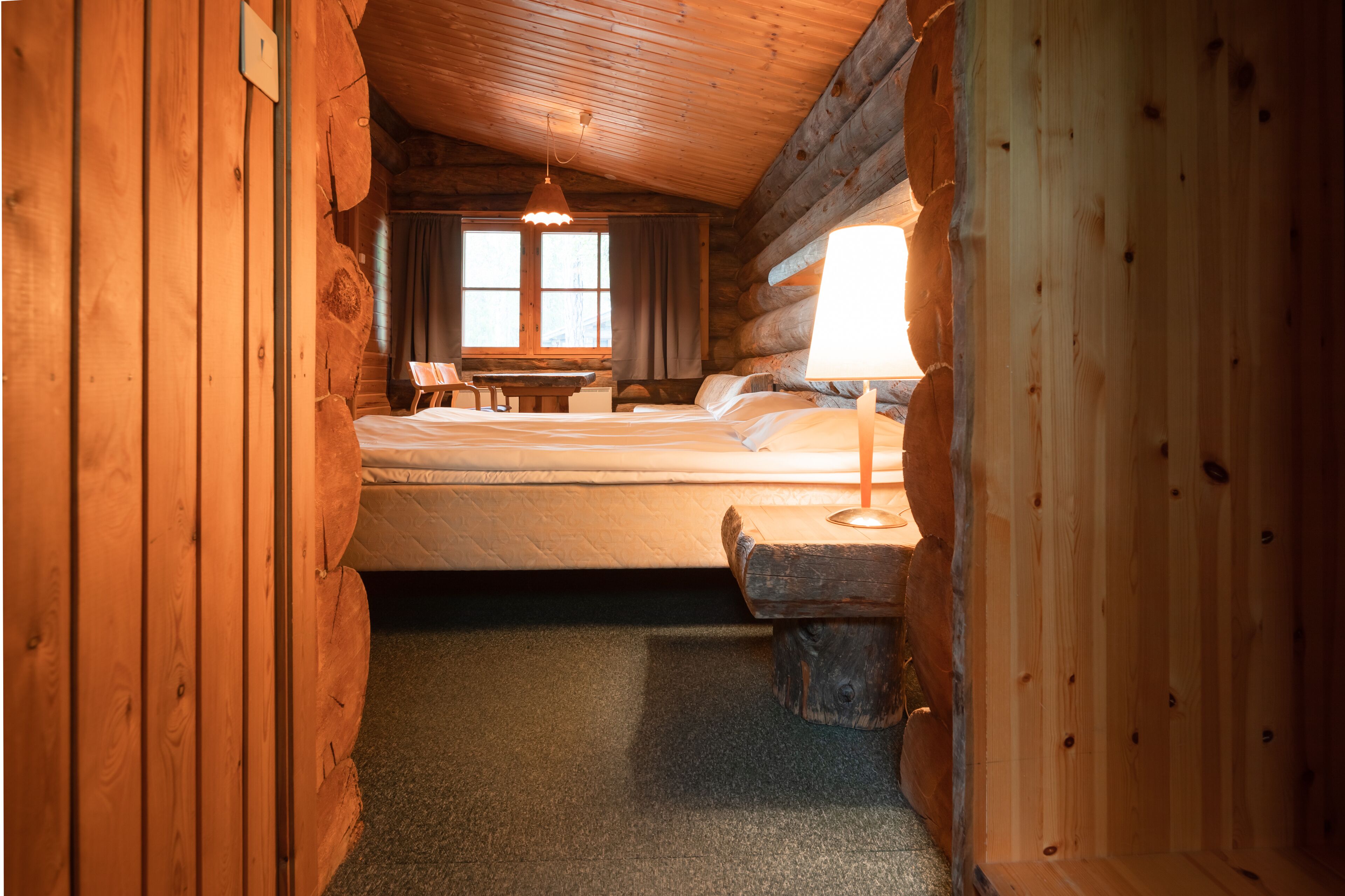 A log cabin bedroom with a bed, bedside lamp, and a wooden table.